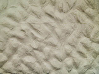 A white wall with a pattern of rocks and a few small holes. The wall is made of concrete plastering...