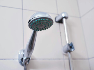 A shower head with a green nozzle is attached to a metal pipe. The shower head is silver and the...