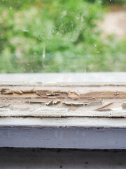 An old wooden window with peeling paint and wood. The window is dirty and has a lot of wood chips...