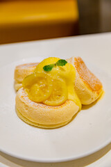 Soufflé pancakes topped with lemon cream, candied lemon slices, and a mint leaf, served on a white plate dusted with powdered sugar