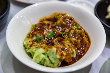 Bowl of vegetable-filled wontons in spicy red chili oil, garnished with scallions and sesame seeds, served in a white bowl for a flavorful spicy bite