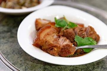Slow-braised pork knuckle with glossy soy glaze and visible bone-in cut, served hot in a deep white bowl with fresh coriander sprigs