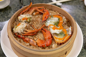 Steamed glutinous rice topped with fresh crab and crab roe, served in a bamboo steamer as a traditional seafood dish called crab rice