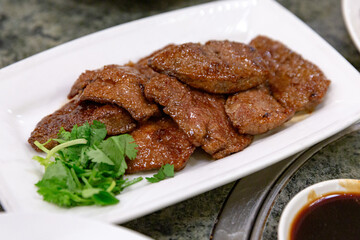 Stir-fried pork liver with scallions, served hot on a white rectangular plate, showcasing tender texture and glossy soy-based sauce