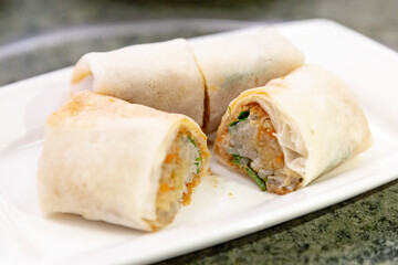 Sliced Taiwanese runbing placed on a white plate, filled with shredded vegetables, crushed peanuts...
