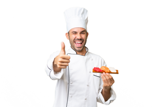 Young caucasian chef holding a sushi over isolated background with thumbs up because something good has happened