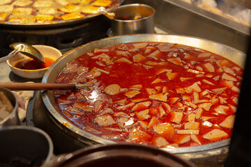 Large metal pan of Taiwanese spicy hot pot base with sliced pig intestines and tofu simmering in rich red chili oil soup at a food stall
