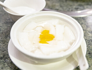 Chinese almond tofu dessert served in a smooth white syrup, topped with canned peach slices in a white porcelain bowl with ceramic spoon