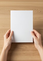 Fototapeta premium Two hands hold a blank white paper sheet on a wood surface