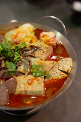 Close-up of Taiwanese spicy hot pot featuring tofu, duck blood, cabbage, and anchovy in chili oil broth with cilantro garnish