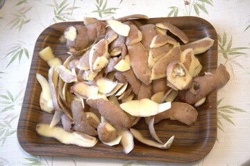 Fresh potato peels on rustic wooden tray prepared for composting, close-up view.