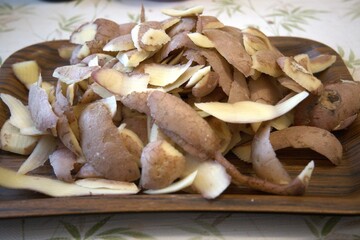Fresh potato peels on rustic wooden tray prepared for composting, close-up view.