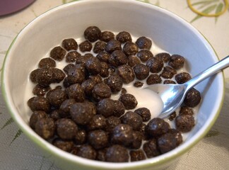 Crispy chocolate cereal balls served with milk in small bowl, nutritious breakfast for children.
