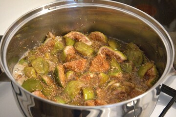 Homemade fig jam boiling in metal pot on stove, close-up preparation process.