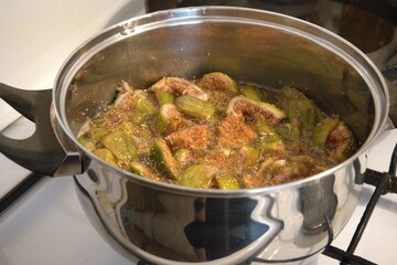 Homemade fig jam boiling in metal pot on stove, close-up preparation process.