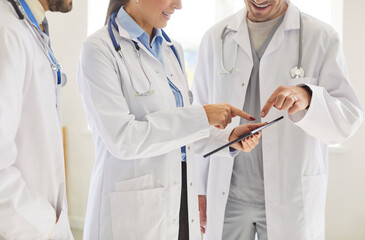 Cropped shot of unknown team of medical workers or doctors wearing white medical coats, using tablet for downloading app to have appointment online, discussing prescription plan for patient