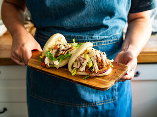 Woman holding wooden board with Bao Buns with pulled chicken and vegetables, close-up