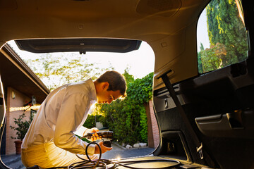 Young man preparing electric vehicle charger in car trunk at sunset