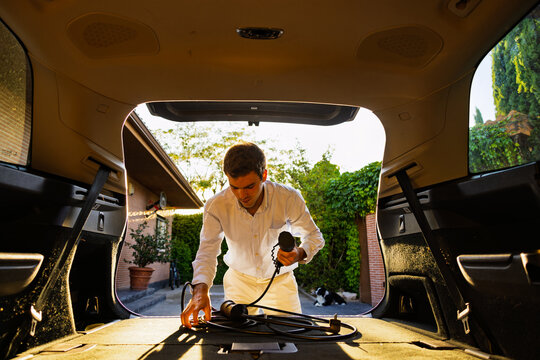 Man taking charging cable for electric car from trunk at home