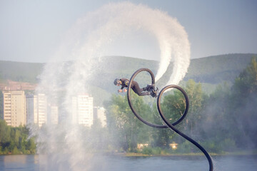 Flyboarding adventure showcasing acrobatics over calm water at sunset near city skyline. An athlete...