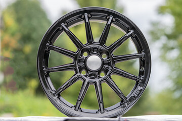 Black multi-spoke alloy wheel cast aluminum disc from a sports car on a green background outdoor...