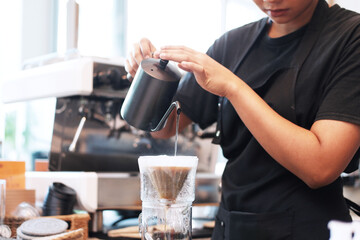 Close up professional Asian woman barista weraing black apron and pouring hot water into the coffee dripper on counter bar in cafe or coffee shop