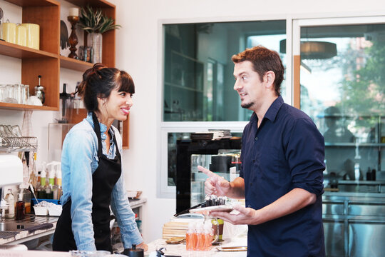 Smiling Caucasian barista woman receiving orders from customers is businessman holding tablet for to choose a menu to order drinks in cafe