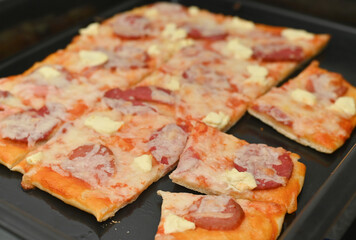 freshly baked pizza with a variety of toppings, including pepperoni, cheese, and vegetables. The pizza is sliced into portions, ready to serve, on a black baking tray.