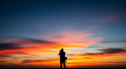 Lone photographer captures stunning sunset sky with vibrant orange and pink hues creating a dramatic silhouette scene