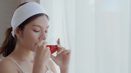 Beautiful young asian woman with headband enjoying tea standing near window with satisfied in living room at home, happy woman drinking tea or beverage for health and relaxation, lifestyle and health. - Powered by Adobe