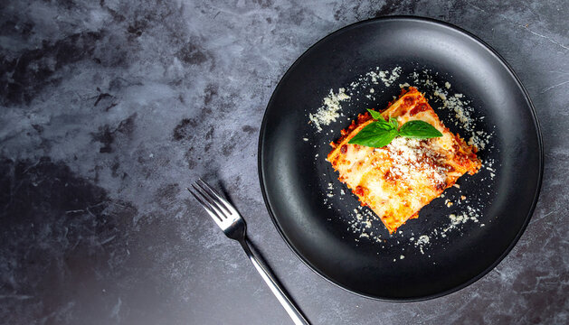 Delicious lasagna on a black plate, ready to be enjoyed