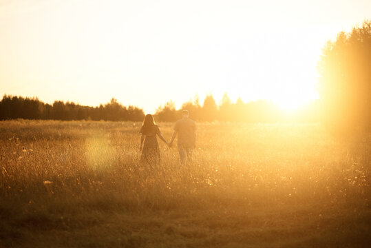 A silhouetted couple enjoys a peaceful sunset walk in a field.