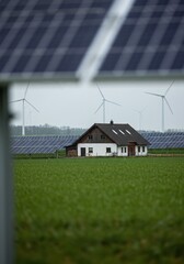 Rural landscape powered by the future a house in green fields, framed by foreground solar panels and distant wind turbines, showcasing sustainable energy solutions