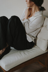 Fototapeta premium Cozy morning with woman lounging on sofa in striped shirt, minimal decor, sunlit relaxed atmosphere