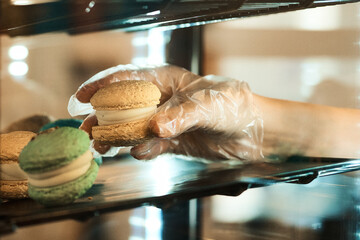 A hand in a glove presenting a delicious macaron from a bakery display case