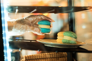A hand holds a blue macaron, part of a colorful dessert display in a cafe.
