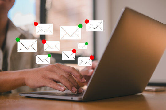 Close-up of hands typing on laptop with email notification icons floating above. Concept of communication, inbox overload, digital marketing, business email, online messaging, and work life.