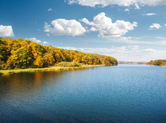 Breathtaking view of the azure lake surrounded by forest in sunny autumn weather.