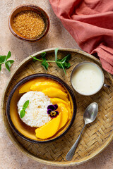 Thai mango sticky rice with coconut milk, garnished with edible flowers and mint on light background top view vertical photo