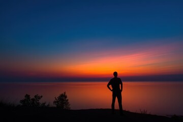 A person stands by a calm lake, gazing at a vibrant sunset with colorful skies and peaceful reflections on the water