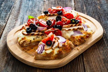 Pinsa Romana with grilled chicken breast, mozzarella cheese, tomatoes and black olives on wooden table	