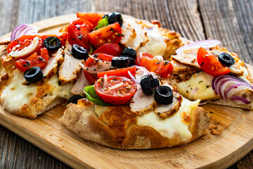 Pinsa Romana with grilled chicken breast, mozzarella cheese, tomatoes and black olives on wooden table	