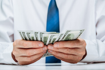 well-dressed person carefully counts stack cash while sitting at desk in professional office. concept investment, success, financial prospects and career growth. focus is on money in hand. close up.