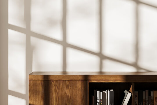 Minimalist wooden bookshelf with books in warm sunlight casting soft window shadows on beige wall, ideal for interior design product mockup display. 3D Rendering