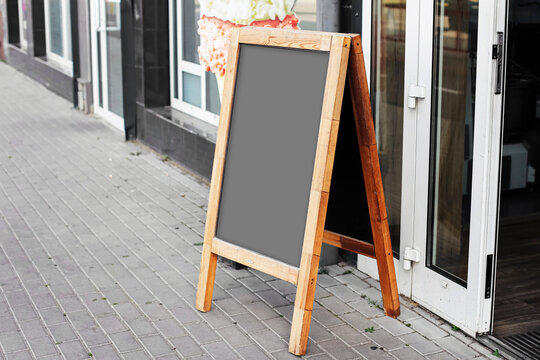 Wooden street chalkboard stand. Blank menu board in front of cafe entrance. Empty outdoor sign ready for text or restaurant offer. Urban sidewalk advertising concept. Marketing space for promotion.
