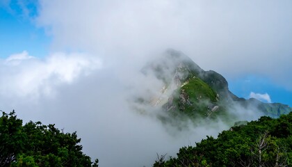 Lush green mountain peak shrouded in white and gray clouds against a vibrant blue sky.