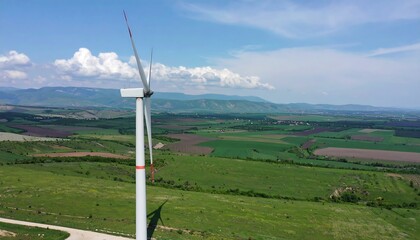 High-angle view of a wind turbine atop a rolling, verdant landscape, with a distant valley and mountains.