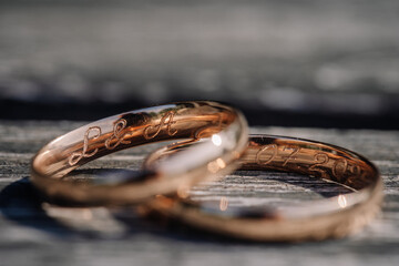 Close-up of two engraved gold wedding rings resting on wooden surface, with initials “L & A” and a date visible, symbolizing love and commitment.