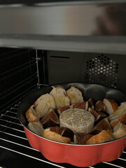 Round baking pan in the oven with bread, figs, and a wheel of cheese prepared for baking.