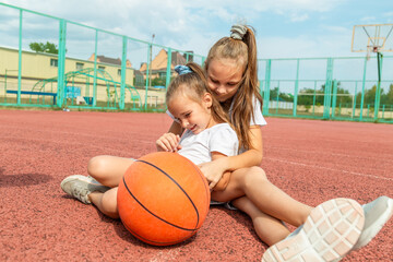 Tickling and fun. little girls sisters lying on the rubber surface of a sport court outdoors after play basketball. Concept of sport, active lifestyle. Sports and recreation